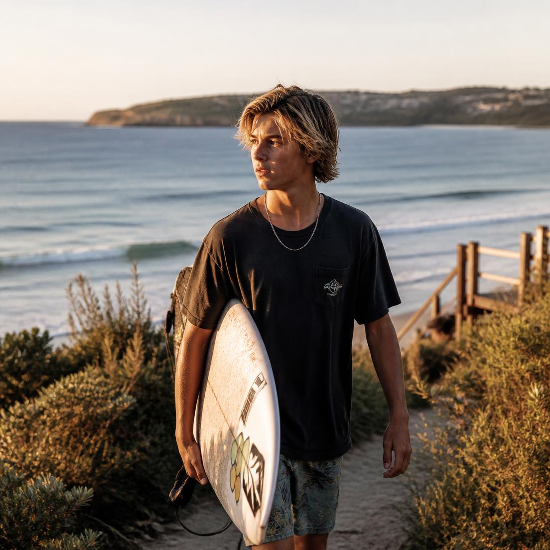 Young Australian surfer walking a beach path at golden hour